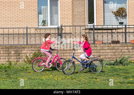 Two girls ride a bicycle. Two sisters ride a bicycle on the lawn in front of the house Stock Photo