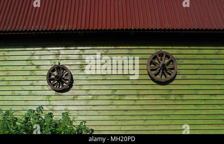 Two ancient wooden rustic wagon wheels from carriage hangs on wall of wooden house. Two vintage circle from cart on wall of old log house. Old retro h Stock Photo