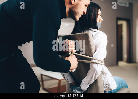 Robber maniac tied female victim to a chair Stock Photo