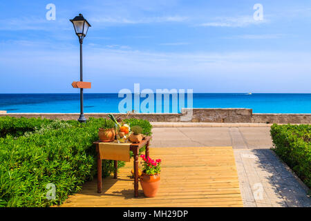 Pot with flowers and restaurant table decorated with vegetables on wooden deck along seashore in small village near Cala Ratjada, Majorca island, Spai Stock Photo