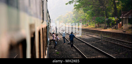 Opportunistic vendors selling supplies to passengers from the tracks through the windows of a stopped train, India Stock Photo