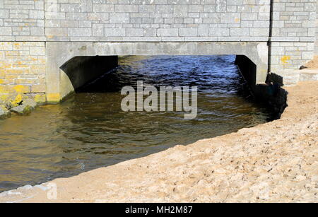 Small river flowing under a stone bridge and past a sandy beach on its way to the nearby sea. Stock Photo