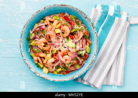 MEXICAN FOOD. Mexican shrimps ceviche sebiche with tomatoes and avocado in blue bowl, wooden blue background. Top view. Stock Photo