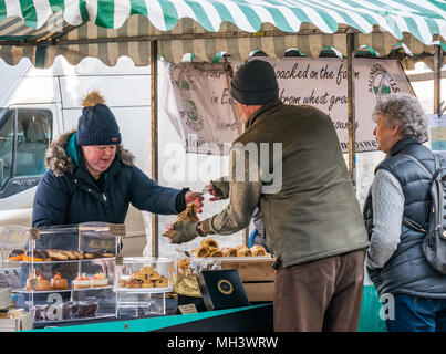 Man buying cakes at outdoor market stall, Haddington Farmers Market, Place d'Aubigny, Court Street, East Lothian, UK on Winter day Stock Photo