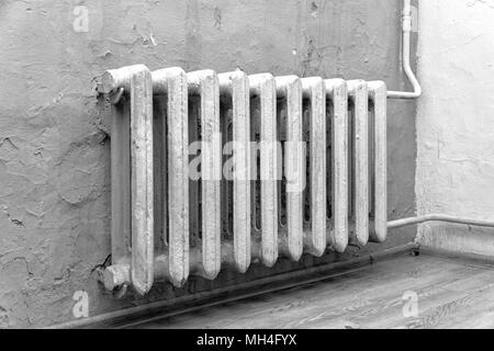 Old cast-iron radiator on the background of gray wall. Black and white photo Stock Photo