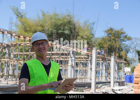Engineers wear a helmet and holding construction plan and tablet monitoring the construction area. Stock Photo