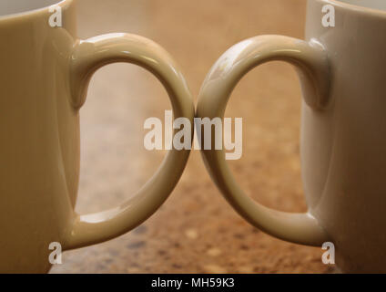 two coffee cup handles touching each other over a marbled countertop Stock Photo