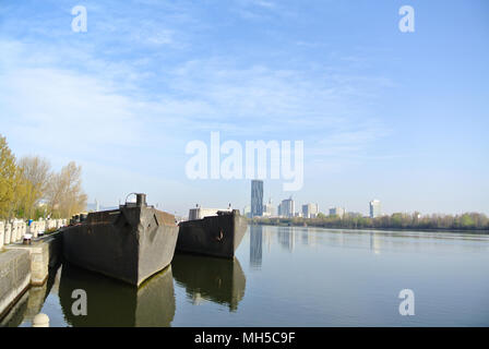 Danube river in early morning under light blue sky. Two big barges moored on the river bank. The other side have modern skyscraper and reflection Stock Photo