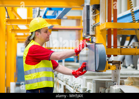 Worker in a factory pressing a red button. Worker wearing yellow reflective suit, yellow helmet and red working gloves Stock Photo