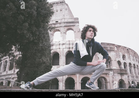 Handsome young sportsman stretching and warming-up for training in front of Colosseum in Rome Stock Photo