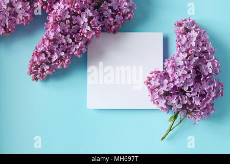 Sprigs of purple lilac with paper card note on light blue background. Copy space. Stock Photo