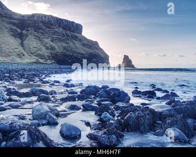 Amazing sunset, Talisker bay on the Isle of Skye in Scotland. Foamy sea, boulders and large cracked rocks with erosion marks. Rocky coastline with sea Stock Photo