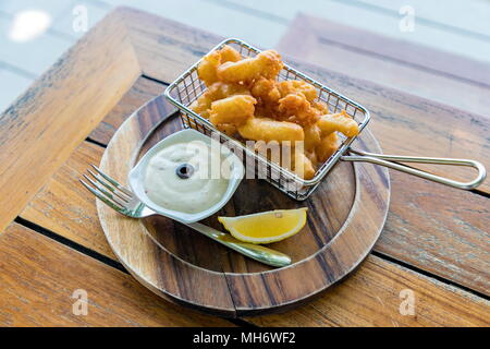 Calamari (Crispy Squid) with sauce and lemon in wooden plate with a fork on the wooden table. Selective focus. Stock Photo