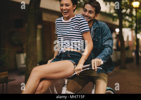 Man riding bicycle with his girlfriend sitting on handlebar. Couple having fun while riding bicycle. Stock Photo