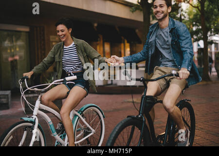 Happy young couple holding hands and riding on bikes. Smiling man and woman cycling together in the city. Stock Photo