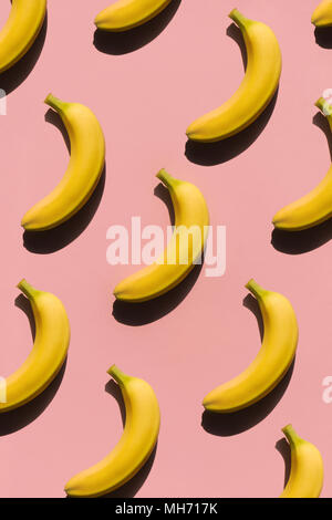 Flat lay of arranged yellow bright bananas in seamless pattern on light pink surface. Stock Photo