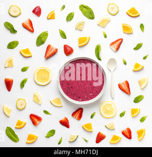 Flat lay of bowl with delicious red smoothie on white surface with arranged pieces of fruit and mint leaves. Stock Photo