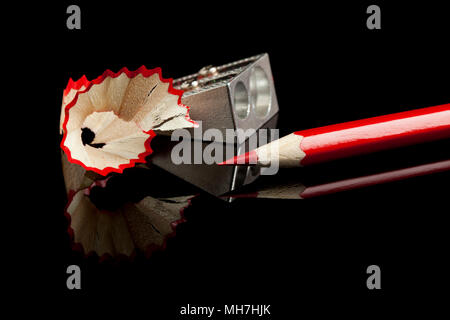 sharpened red pencil  with sharpener and shavings on reflective black surface Stock Photo