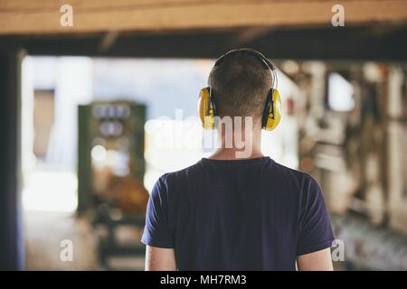 Man working in sawmill. Rear view of the worker with headset. Stock Photo