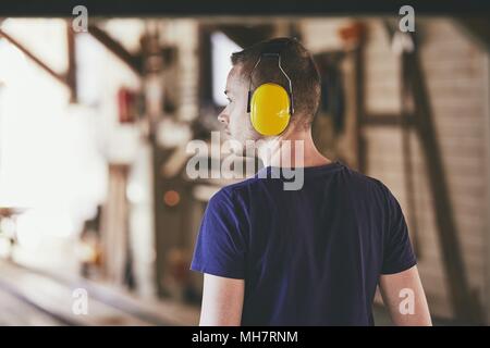 Man working in sawmill. Rear view of the worker with headset. Stock Photo