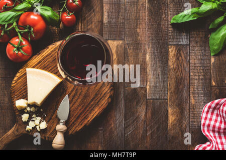 Parmesan cheese, tomatoes, basil and glass of red wine. Italian food. Rustic italian food on wooden background. Cheese and wine. Top view Stock Photo