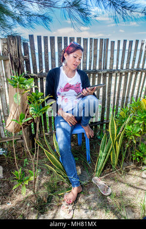 A Filipino woman sits at a beach resort having a voice call using her iPad and the internet in Palawan, Philippines. Internet availability is good thr Stock Photo