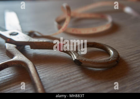 Old metal scissors and tailor measure tape on grey wooden background. Retro sewing accessories for home sewing and repair of clothing. Stock Photo