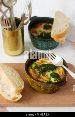 Baked scrambled eggs with broccoli, sausages and cheese served with slices of bread. Rustic style, selective focus. Stock Photo