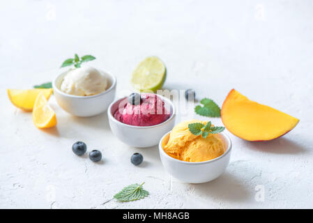 Three various fruit and berries ice creams on white background, copy space. Frozen yogurt or ice cream with lemon, mango, blueberries - healthy summer Stock Photo