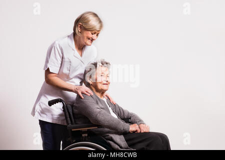 Studio portrait of a senior woman in wheelchair and a nurse. Stock Photo