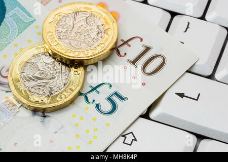 Sterling five and ten pound notes and 2 new pound coins pounds GBP money on a keyboard with enter key. Online investing / shopping concept. England UK Stock Photo