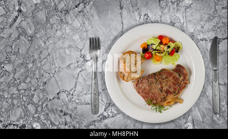 Ripened seasoned beef rump or striploin steak cooked on white plate with salad and home made bread. Top view on granite background with copy space. Stock Photo