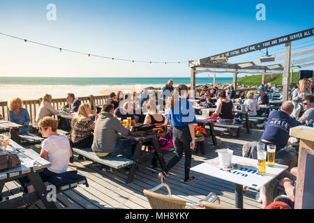 Holidaymakers on a staycation holiday relaxing on the terrace of the Fistral Beach Bar and enjoying the evening sunlight. Stock Photo