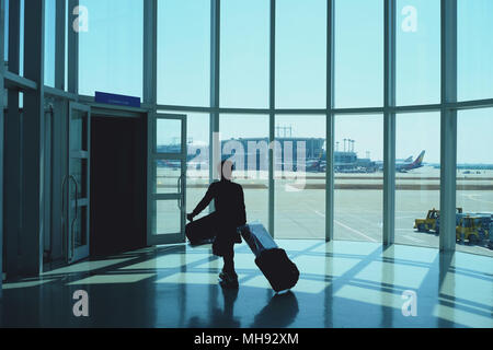 Woman dragging a small carry on luggage at airport corridor walking to departure gates silhouette Stock Photo