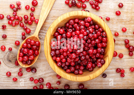 Ripe cranberries in a wooden plate and scattered side by side on a wooden table, top view Stock Photo