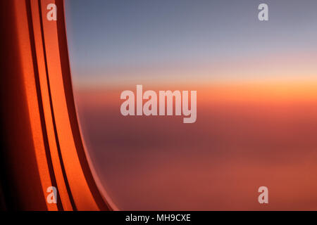 View through airplane porthole of purple sunset in sky Stock Photo