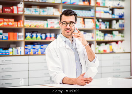 Young friendly male pharmacist with smartphone, making a phone call. Stock Photo