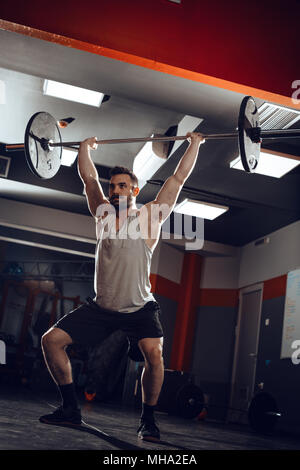 Young muscular man lifting a barbell at the gym. He doing overhead squat exercise with barbell on cross training. Stock Photo