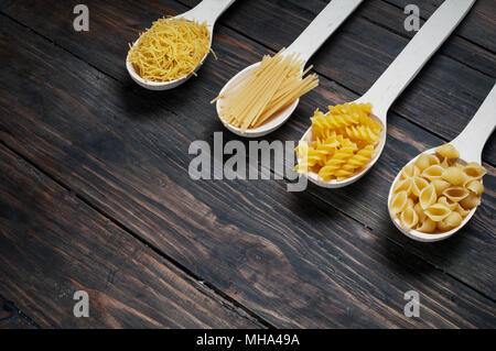 Various mix of pasta on wooden rustic background, sack and spoons. Stock Photo