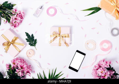 Festive composition of purple flowers, gift boxes with golden ribbons, mobile phone with blank screen and green leaves on a white table top view Stock Photo