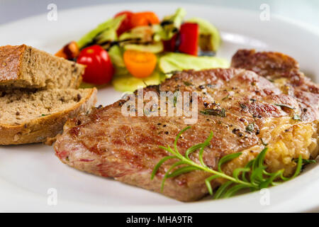 Ripened seasoned beef rump or striploin steak cooked on white plate with salad and home made bread Stock Photo