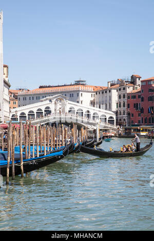 Gondolas in front of Rialto bridge, on the Grand Canal,  Venice, Veneto, Italy with a golndolier returning his boat to its mooring and tourists on the Stock Photo