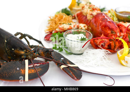 Live and cooked lobster served with the vegetables on a white plate. Isolated Stock Photo