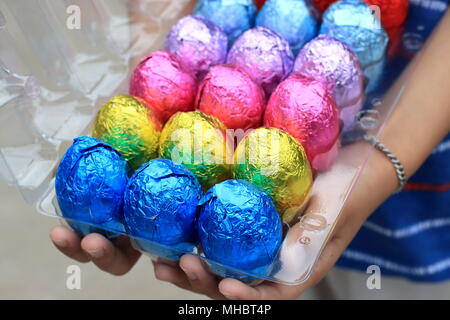 Hand holding Colourful Chocolate Eggs on plastic carton Stock Photo