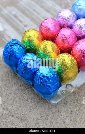 Hand holding Colourful Chocolate Eggs on plastic carton Stock Photo