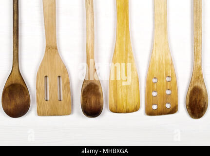 Row of wooden kitchen tools with spoons and spatulas from above on white wooden board background Stock Photo