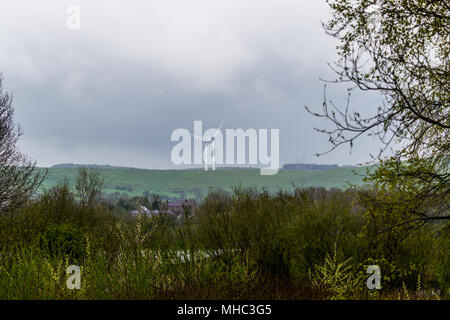 A windfarm visible through the trees standing on top of a hill Stock Photo