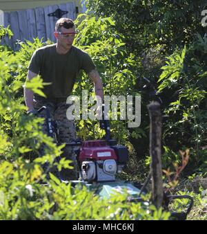 Corporal Jacob Cummings, a fire team leader with 2nd Light Armored Reconnaissance Battalion, mows down bushes while participating in a community service event as part of Navy Week New Orleans, April 23, 2018, April 23, 2018. During Navy Week New Orleans, Marines and Sailors are dedicated to supporting communities. (U.S. Marine Corps photo by Lance Cpl. Samuel Lyden). (U.S. Marine Corps photo by Lance Cpl. Samuel Lyden). () Stock Photo