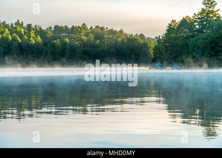 Solitude as the early morning mist lifts off the bay exposing docks and cottage life Stock Photo