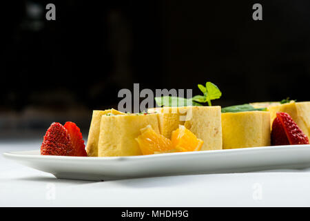 Rolls of thin pancakes with smoked salmon, horseradish cream cheese and rocket leaves on white plate on black background Stock Photo